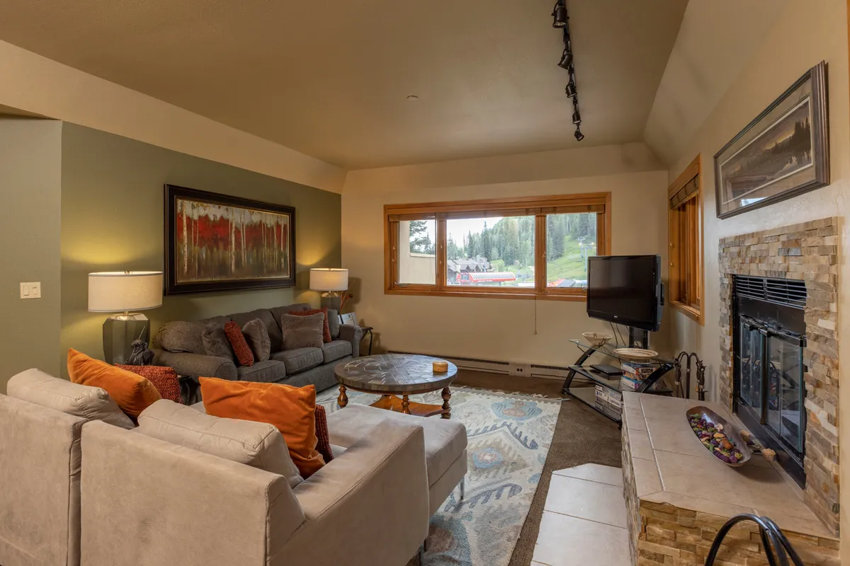 A sophisticated living area featuring comfortable sofas, a prominent fireplace, and a large window framing stunning mountain vistas. Artistic accents and a coffee table set the stage for group activities, from relaxed conversations to board games or quiet moments watching the sunset.