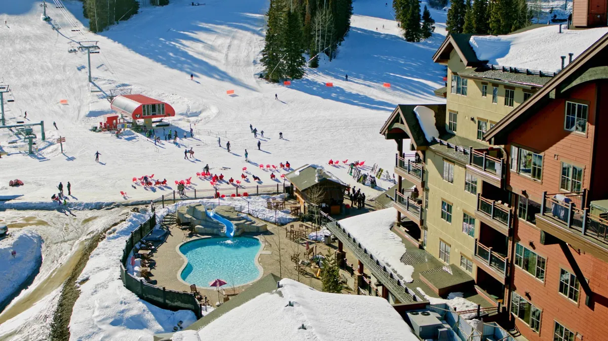 An exterior shot showcasing active ski slopes, a ski lift in operation, a nearby indoor pool, and a residential building nestled among snow-covered trees. The scene conveys both the thrill of the slopes and the relaxation options nearby.