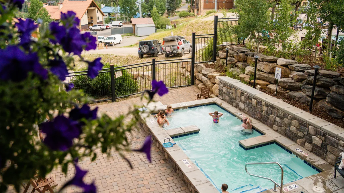 A vibrant scene featuring a swimming pool and adjacent hot tub, surrounded by lush landscaping. People are shown enjoying various activities—swimming, relaxing in the hot tub, and socializing poolside—emphasizing the lively, inviting vibe of the resort.