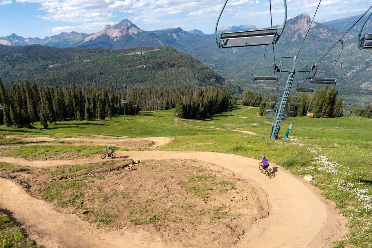 A dynamic exterior shot of a mountain range with winding bike trails, cyclists in action, and an operational ski lift. The image exudes energy and freedom, inviting viewers to imagine themselves hiking, biking, or enjoying scenic rides as a family.